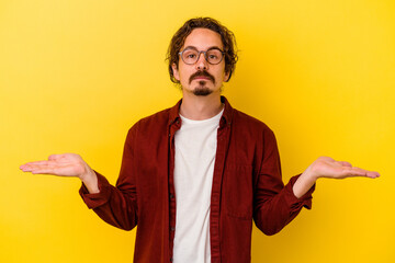 Young caucasian man isolated on yellow background doubting and shrugging shoulders in questioning...