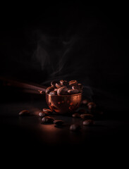 Roasted coffee beans in the copper spoon with smoke on dark background. Concept to recognize the aroma of coffee.