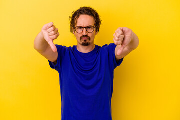 Young caucasian man isolated on yellow background showing a dislike gesture, thumbs down....