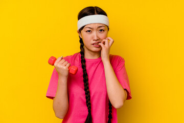 Young sport chinese woman isolated on yellow background biting fingernails, nervous and very anxious.
