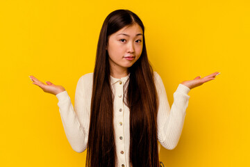 Young chinese woman isolated on yellow background confused and doubtful shrugging shoulders to hold a copy space. - obrazy, fototapety, plakaty