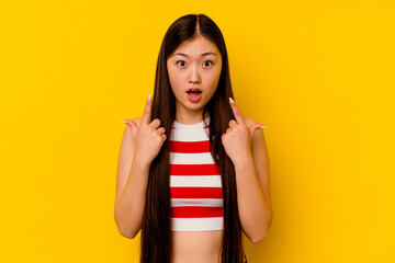 Young chinese woman isolated on yellow background pointing upside with opened mouth.