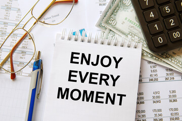 Notebook with text Enjoy Every Moment near office supplies.