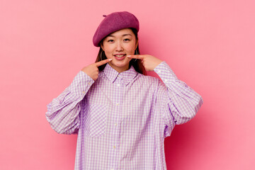 Young chinese woman isolated on pink background smiles, pointing fingers at mouth.