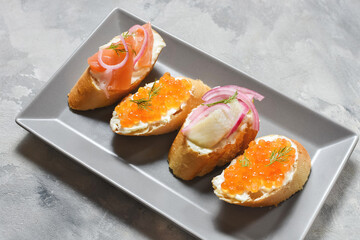 Bruschetta assortment with baguette, cream cheese, red caviar, salmon, herring and onion served on concrete background. Set of appetizers with various toppings