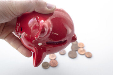 A man's hand holds a red piggy bank and shakes out euro coins from it. Light background. The concept of finding money, crisis, poverty