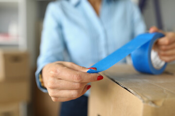 Close-up of female packs up things in carton boxes with blue scotch