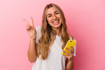 Young blonde caucasian woman holding a yellow mobile phone isolated joyful and carefree showing a...