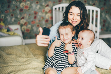 Happy mother with her kids are making a selfie or video call to father or relatives in a bed.