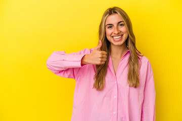 Young blonde caucasian woman isolated on yellow background smiling and raising thumb up