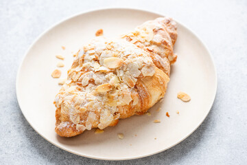 Almond croissant on a plate closeup view. Sweet french pastry baked croissant with almond flakes and powdered sugar