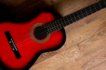 Red-black classical guitar standing on wooden floor