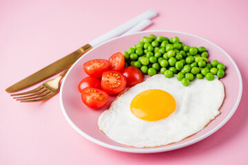 Sunny side up fried egg with green peas on a pink background, closeup view. Breakfast food