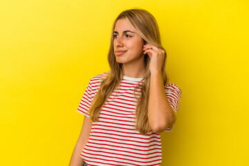 Young blonde caucasian woman isolated on yellow background covering ears with fingers, stressed and desperate by a loudly ambient.
