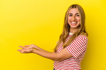 Young blonde caucasian woman isolated on yellow background holding a copy space on a palm.