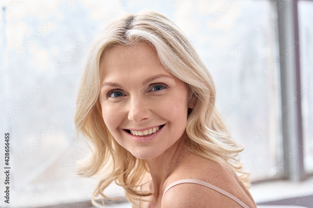 Poster Happy mature elder 50s woman indoors. Closeup headshot portrait of attractive mid age woman looking smiling at camera. Beauty, skin care