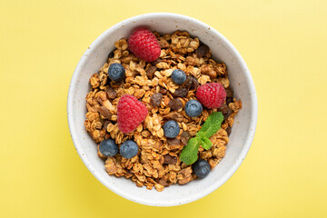 Homemade baked oat granola with fresh berries and raisins in bowl isolated on yellow background. Healthy breakfast cereals, dieting, clean eating concept. Vegan breakfast food
