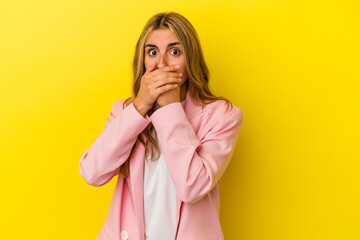 Young blonde caucasian woman isolated on yellow background covering mouth with hands looking...