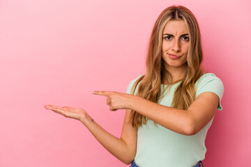Young blonde caucasian woman isolated on pink background excited holding a copy space on palm.