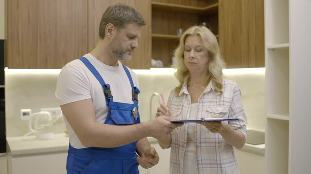 Technician in uniform asking woman to sign invoice, plumbing service, industry