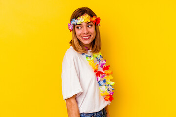 Young caucasian woman celebrating a hawaiian party isolated on yellow background looks aside smiling, cheerful and pleasant.