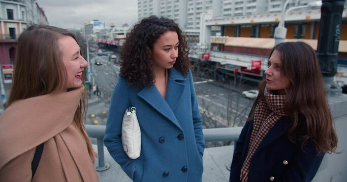 Friendship concept. Beautiful happy diverce women friends cheerfully talk at busy city street bridge, enjoy bonding time
