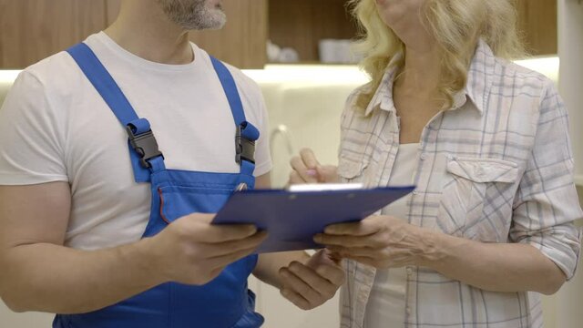 Woman talking to plumber, signing document, house maintenance and repair service