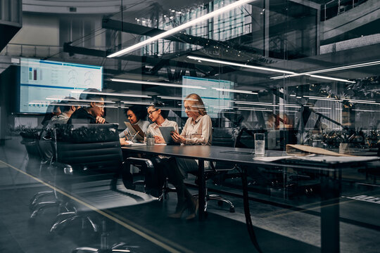 Modern business. Young focused serious business women and men working in a conference room working on a project presentation. Light from a spacious office is reflected through the glass.