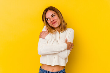 Young caucasian skinny woman isolated on yellow background hugs, smiling carefree and happy.