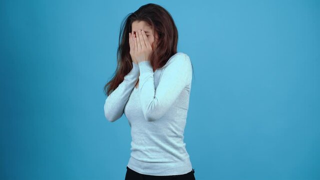 The young brunette, sad, cries desperately with her face in her hands, finally asking for help with her eyes. Asian with dark hair, dressed in a blue blouse, isolated on a dark blue background in the