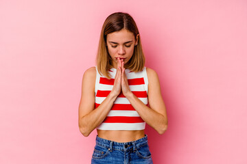 Young caucasian woman isolated on pink background praying, showing devotion, religious person looking for divine inspiration.