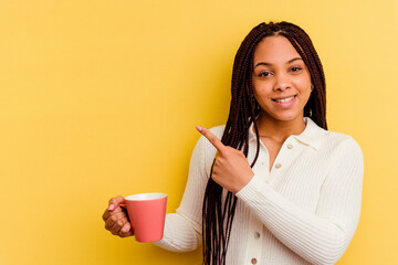 Young african american woman holding a mug isolated smiling and pointing aside, showing something at blank space.