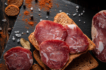 Cured meat on a slate plate. Cold cuts, bread and spices on a wooden table. Products for a sandwich