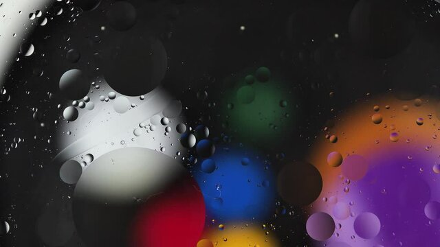 Multi-colored drops of oil floating on the water create a cosmic abstraction.