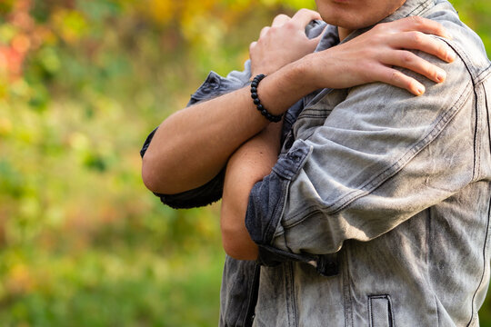 a man stands in a denim jacket with his hands folded in front of him on his chest expressing feelings of concern, anxiety and closeness against the background of a green park copy space close-up
