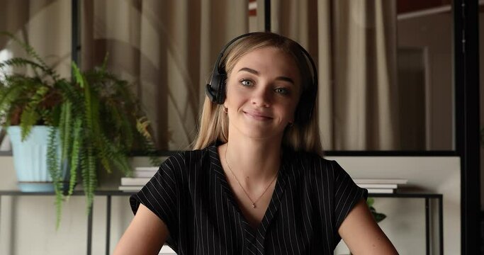 Web camera view smiling young beautiful blonde business lady in wireless headset with microphone looking at camera, holding video call zoom meeting, negotiating working issues with colleagues online.