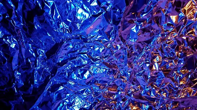 Abstract orange and blue color transition on aluminum wrinkled foil background texture reflecting orange and blue light
