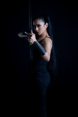 An attractive dark-haired woman in fantasy/urban fantasy style costume holding a bow and arrow and posing against a plain black backdrop