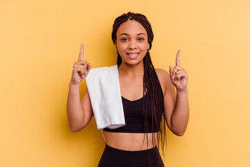 Young sport african american woman holding a towel isolated on yellow background indicates with...