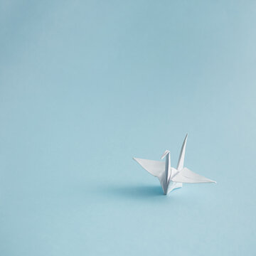 Minimalistic composition of a white origami crane. Orizuru on pastel blue background.
