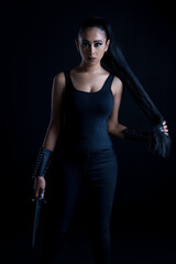 An attractive dark-haired woman in fantasy/urban fantasy style costume and holding a dagger whilst posing against a plain black backdrop