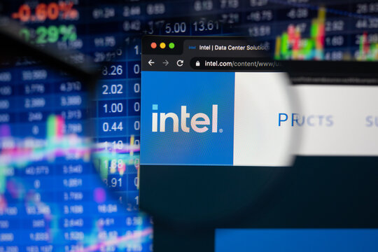 Intel Company Logo On A Website With Blurry Stock Market Developments In The Background, Seen On A Computer Screen Through A Magnifying Glass