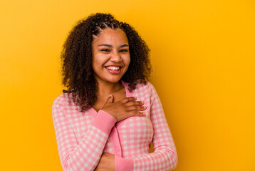 Young african american woman isolated on yellow background laughs happily and has fun keeping hands...