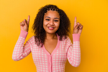 Young african american woman isolated on yellow background indicates with both fore fingers up...