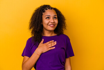 Young african american woman isolated on yellow background laughs out loudly keeping hand on chest.