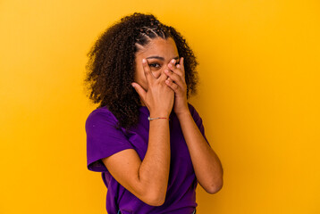 Young african american woman isolated on yellow background blink through fingers frightened and nervous.