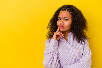 Fototapeta na wymiar Young african american woman isolated on yellow background looking sideways with doubtful and skeptical expression.