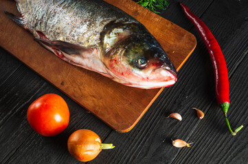 Hypophthalmichthys or bighead carp on a cutting board with vegetables before cooking. Raw peeled fish in restaurant kitchen. Fish diet idea