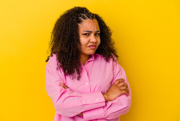 Young african american woman isolated on yellow background frowning face in displeasure, keeps arms...