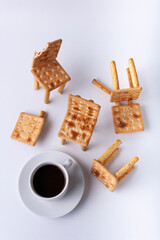 Figures of chairs made of cookies and a cup of black coffee on a white background. Flat lay.